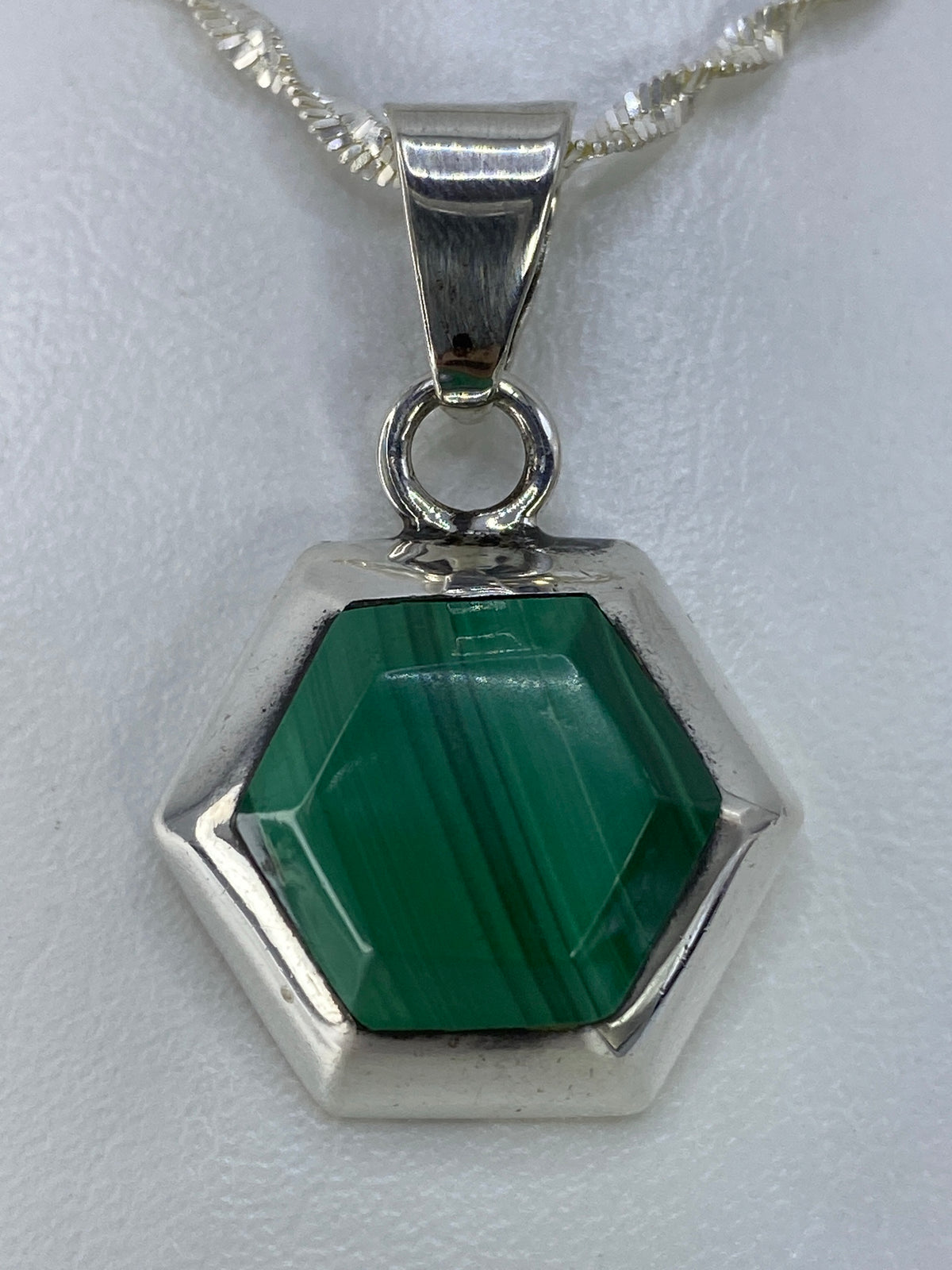 Dije hexagonal de plata 925 con piedra verde engastada a mano, colgando de cadena plateada