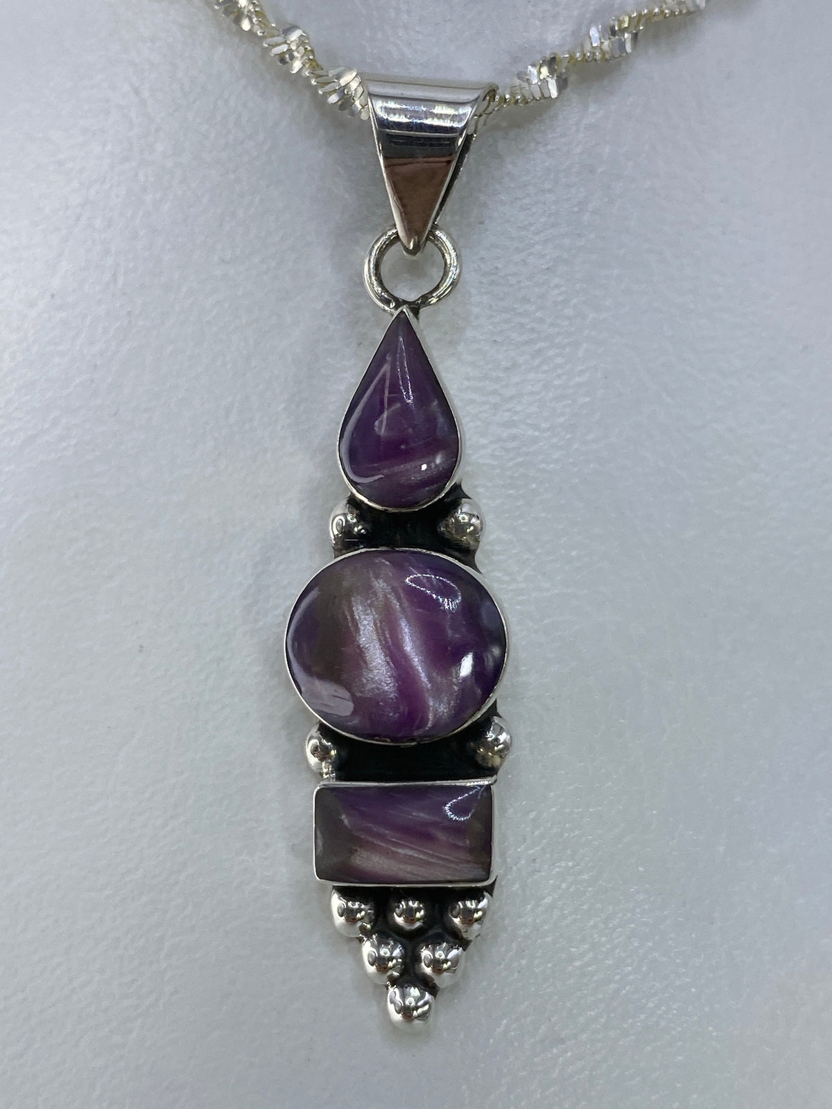 Dije de plata 925 con tres piedras moradas escalonadas colgando del lado derecho