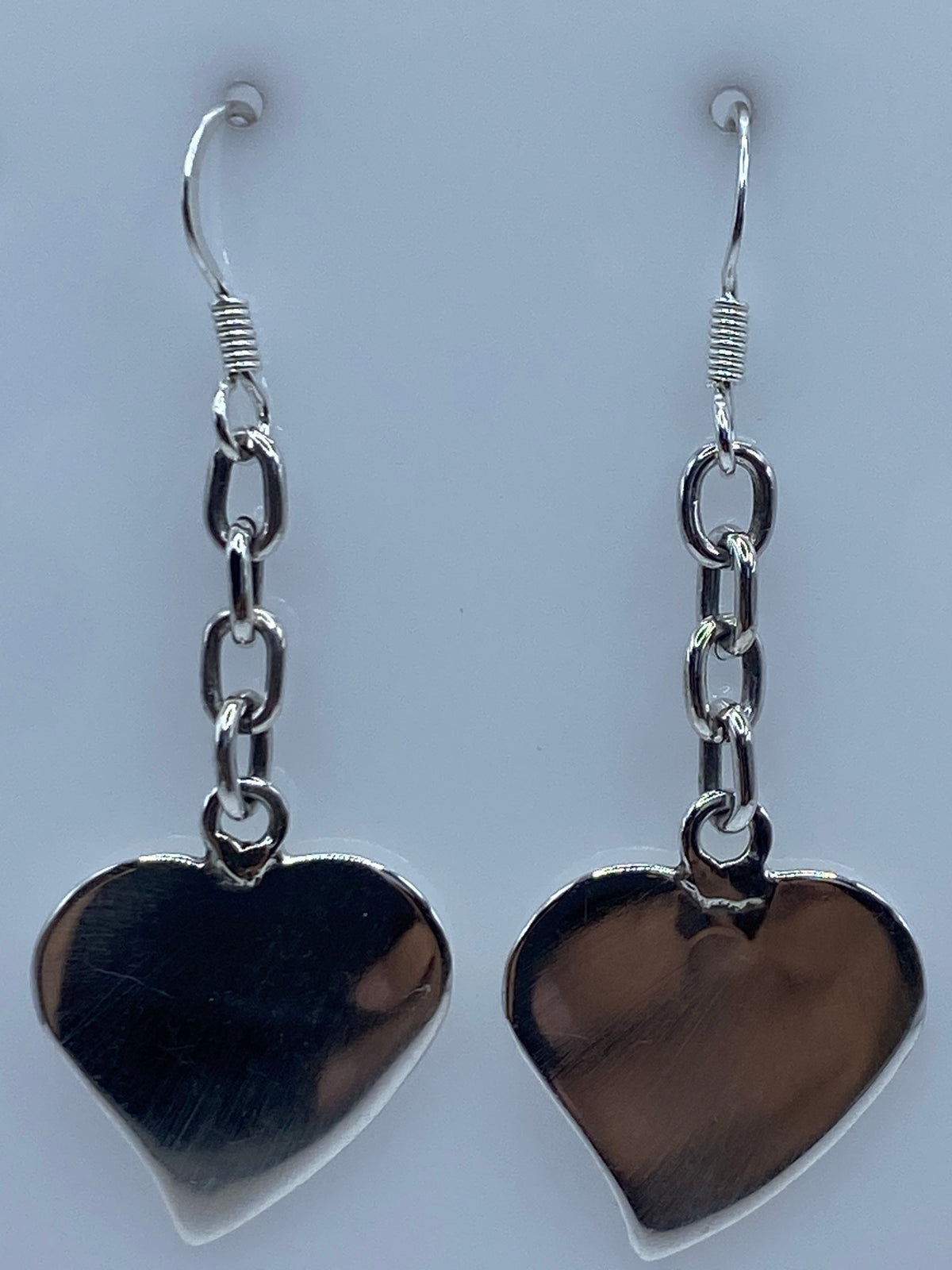 Detalle de un arete de plata corazón mostrando el acabado espejo y el gancho de plata