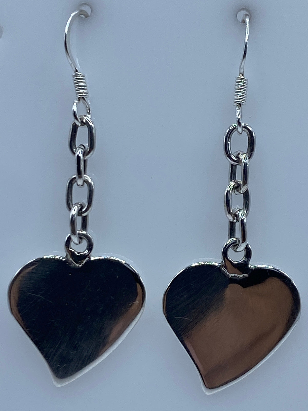 Dos aretes de corazón de plata en una regla de centímetros, mostrando el largo de 5 cm
