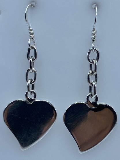 Dos aretes de corazón de plata en una regla de centímetros, mostrando el largo de 5 cm