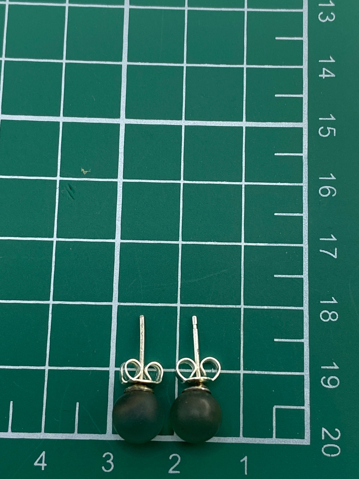 Aretes junto a regla centimétrica mostrando su tamaño compacto de 0.8 cm
