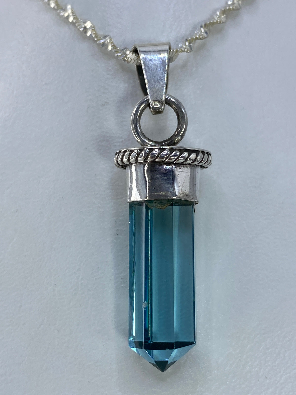 Dije de plata con cuarzo azul cielo engastado a mano, colgando de una cadena de plata