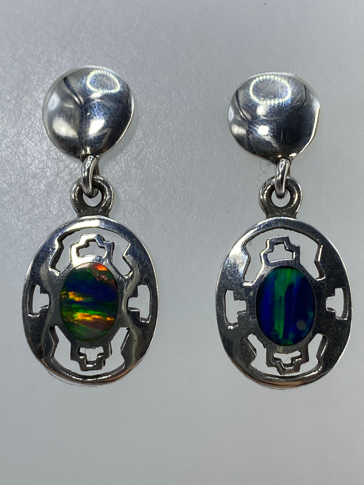 Aretes de ópalo multicolor sobre fondo blanco mostrando el brillo y reflejo de luz