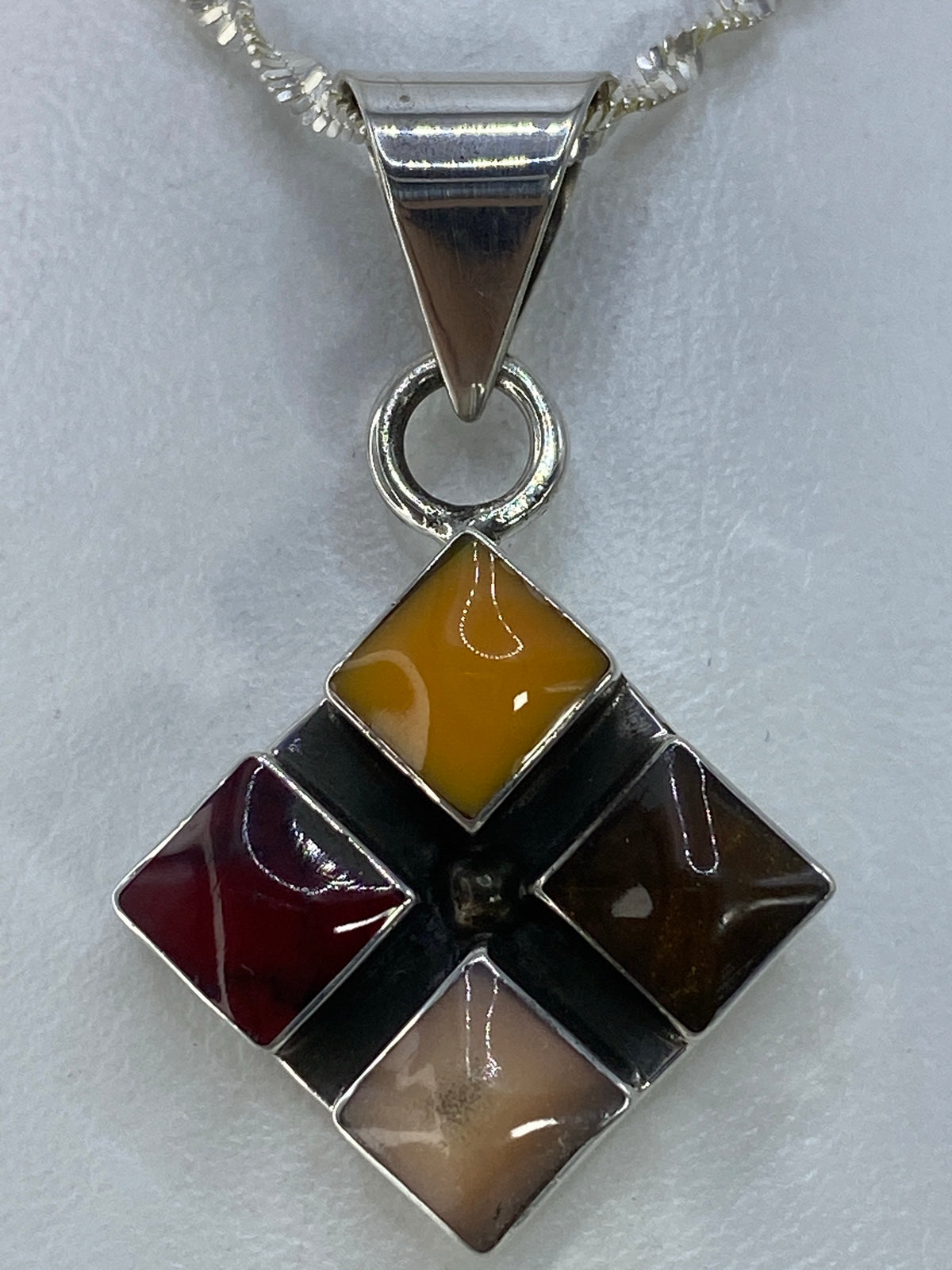 Dije de plata con cuatro piedras de colores: ambar, granate, café y gris en forma de diamante rotado