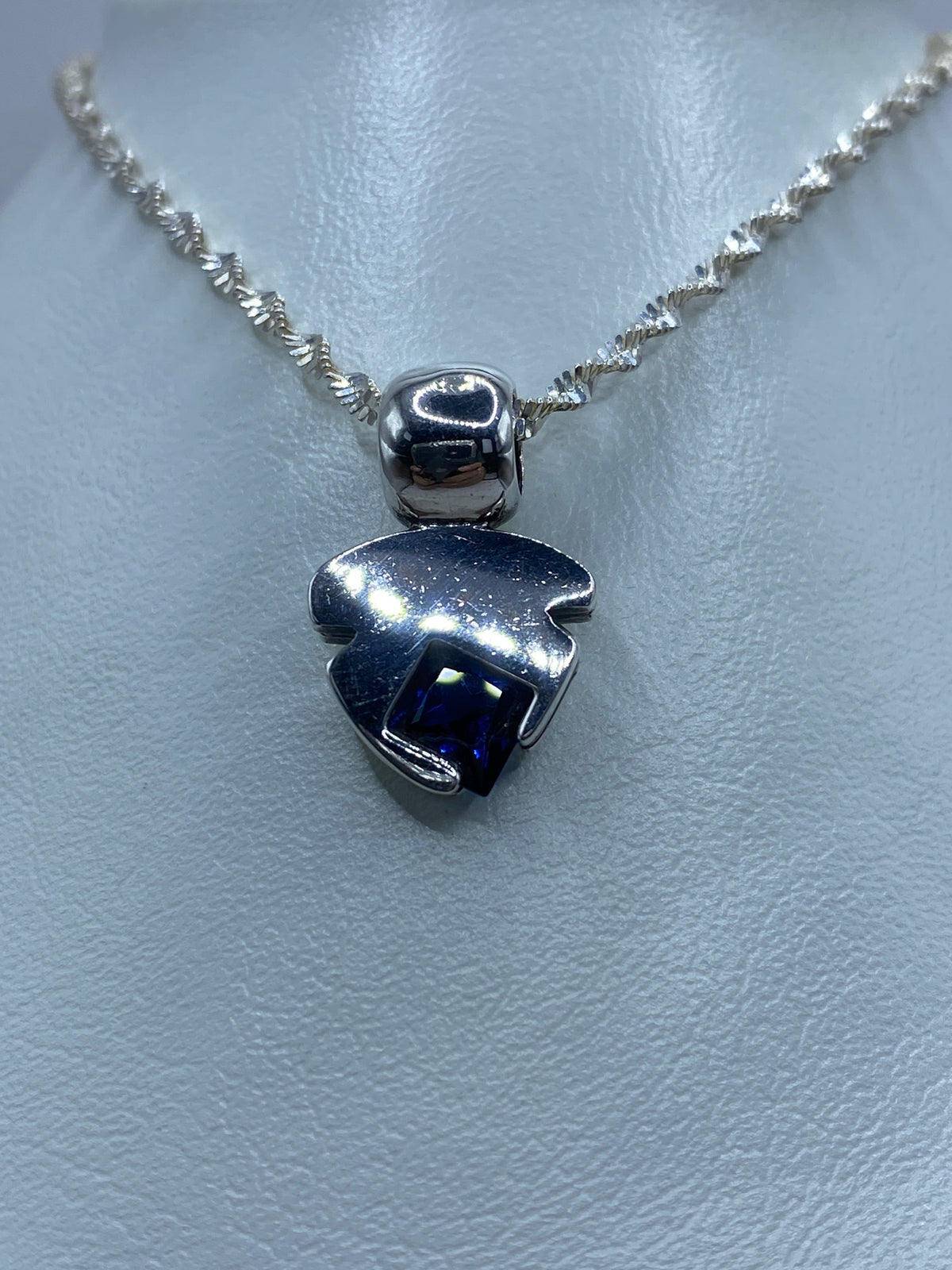 Vista frontal del dije: plata pulida con piedra azul engastada