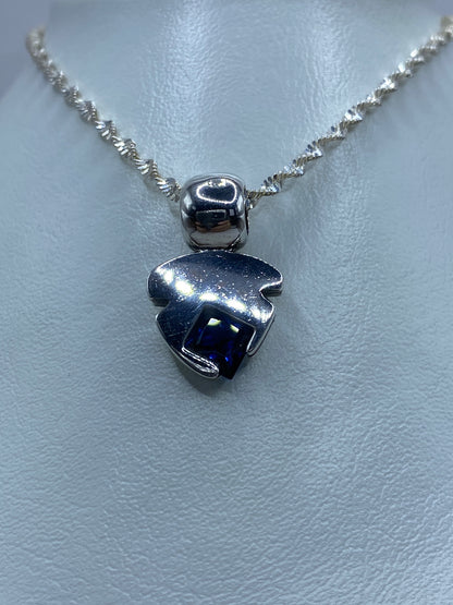 Vista frontal del dije: plata pulida con piedra azul engastada