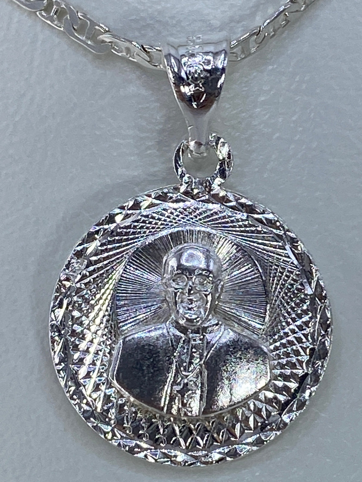 Dije de plata repujado con retrato en relieve y halo radiante, vista frontal