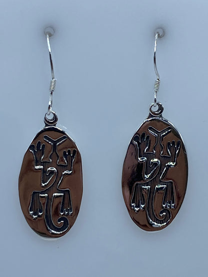 Aretes de plata repujados con motivos prehispánicos colgando del gancho