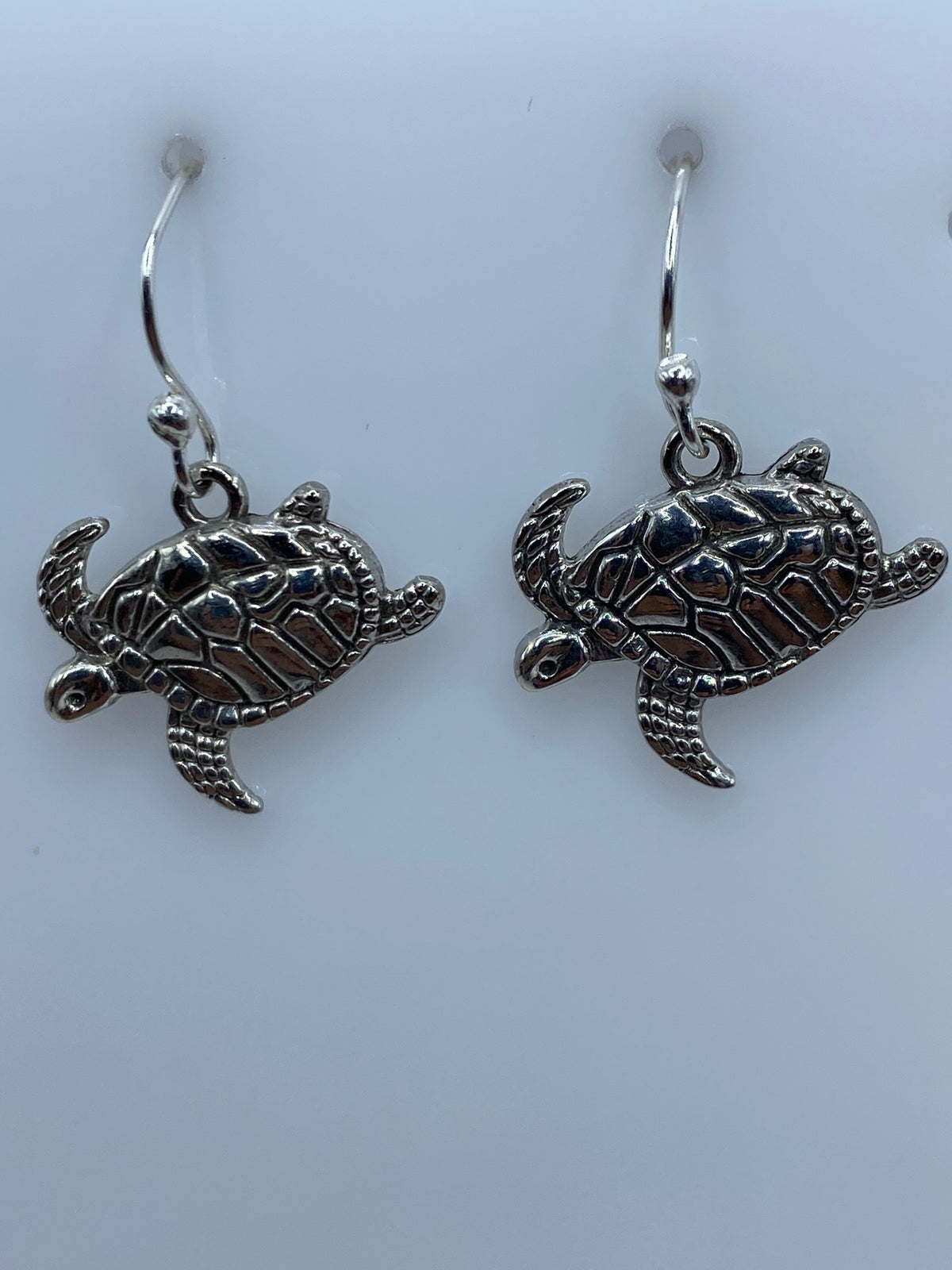 Aretes de plata con tortuga marina en relieve, par completo sobre fondo blanco