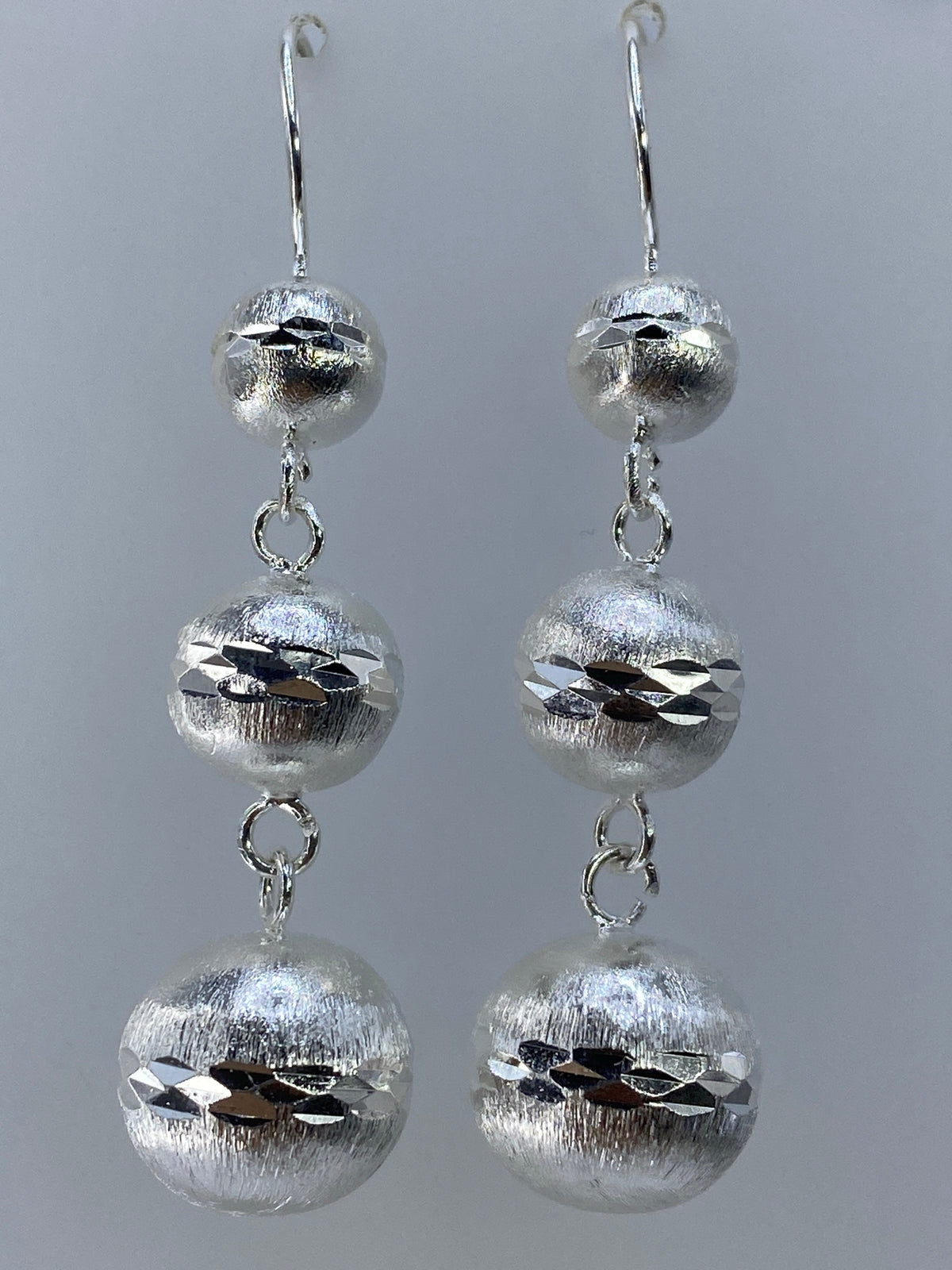 Aretes largos de plata texturados con cortes geométricos en la oreja de una mujer