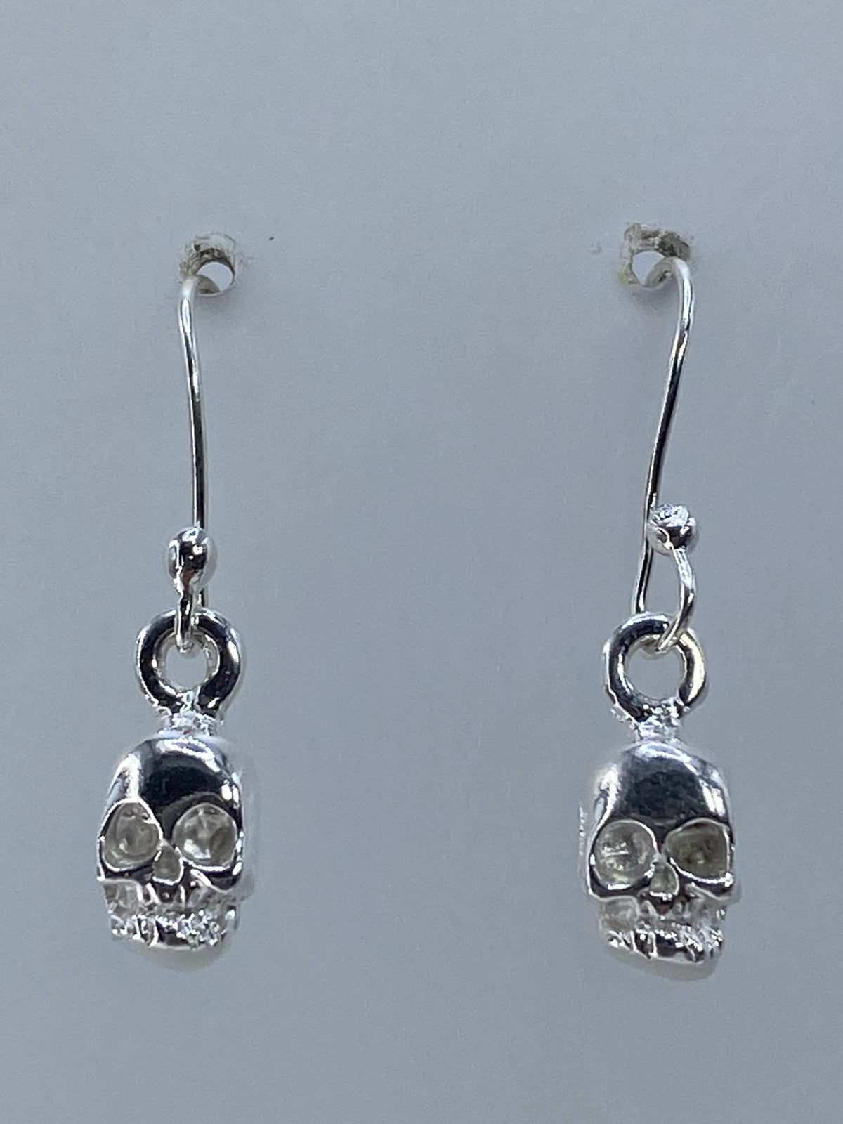 Par de aretes de plata con calavera repujada, largo 2.5 cm, en gancho plateado