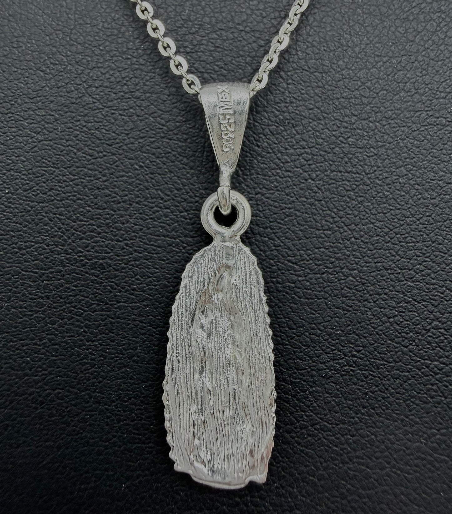 Detalle del dije de Virgen Guadalupe en relieve, fundido en plata pura, mostrando la iconografía tradicional