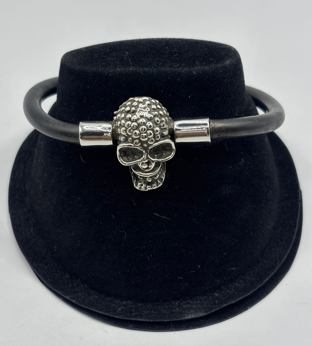 Pulsera de plata .925 con calavera relieve y caucho negro, sobre soporte de terciopelo negro — vista frontal