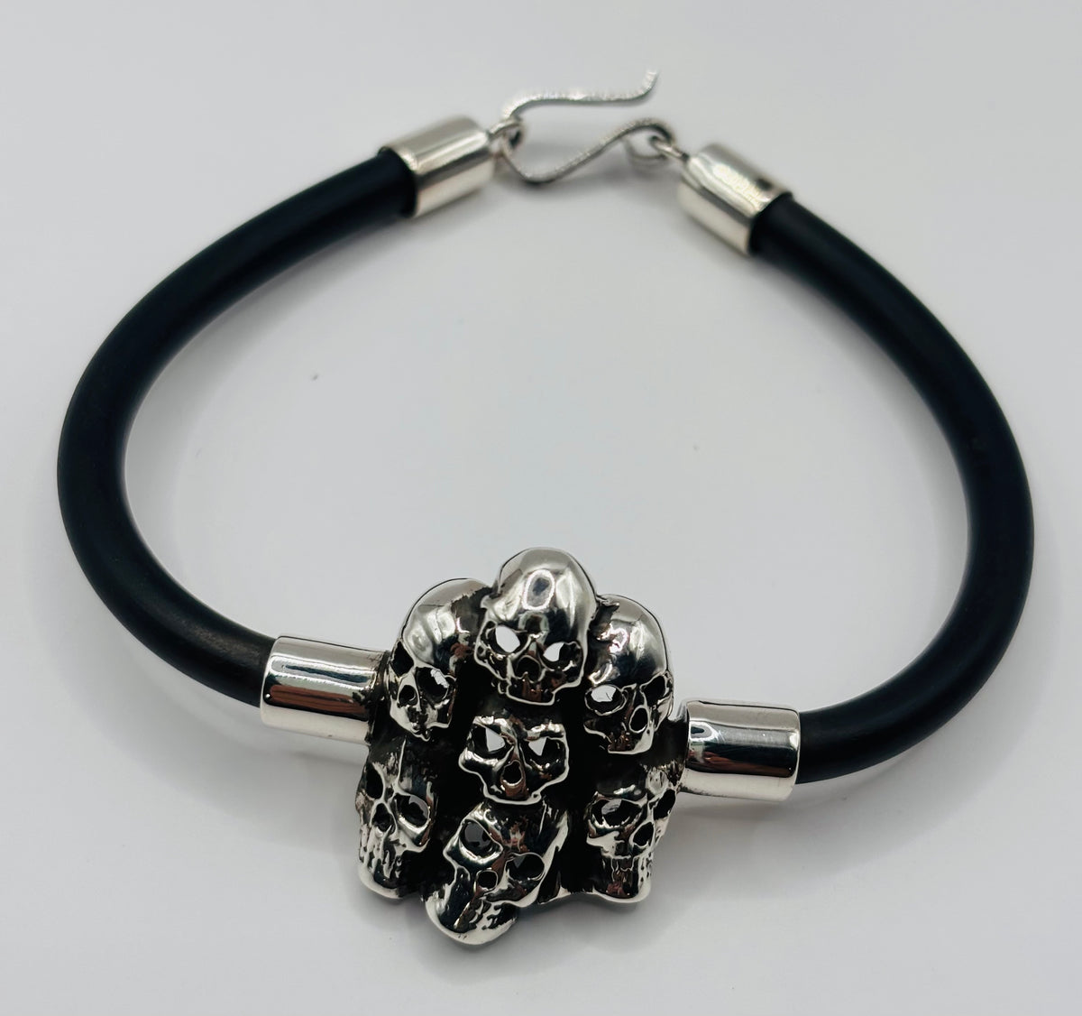 Detalle frontal de pulsera de calaveras fundidas en plata maciza, diseño rebelde y contemporáneo con banda de caucho resistente