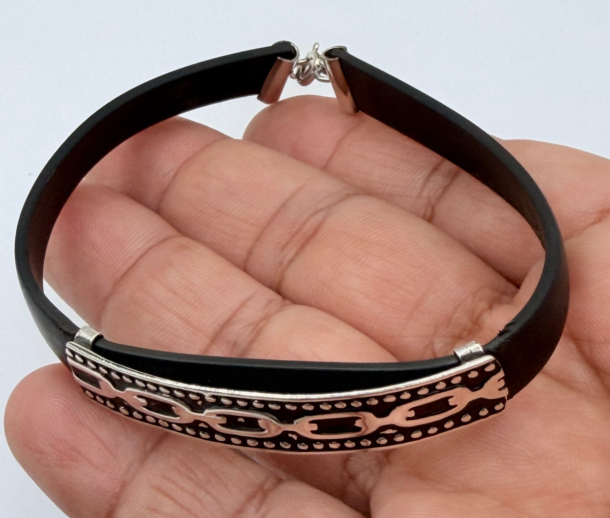 Detalle de las grecas plateadas grabadas en la pulsera, sostenida en mano
